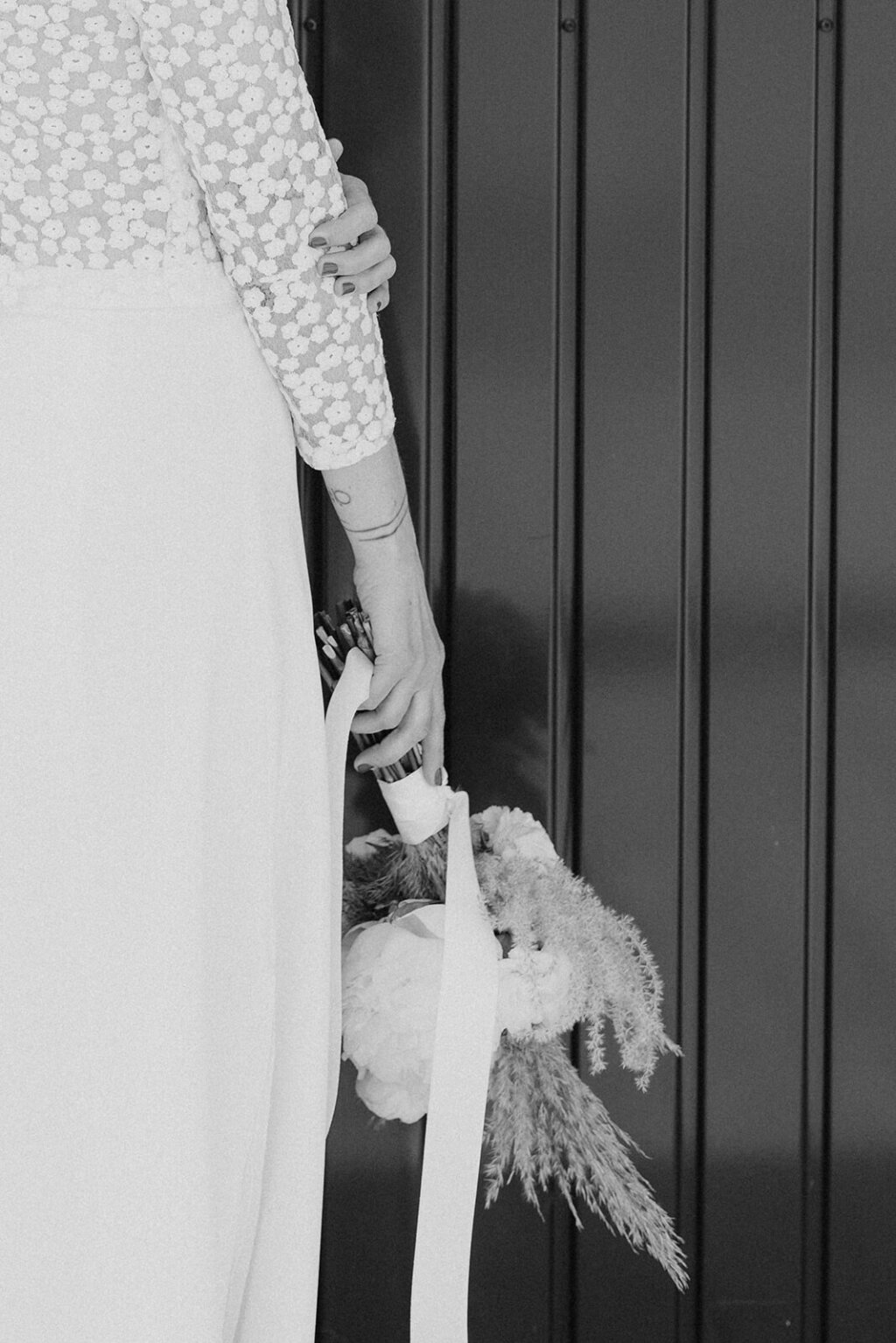 Eine Braut lässt ihren Brautstrauß in der linken Hand locker hängen. Der Brautstrauß besteht aus Trockenblumen und weißen Pfingstrosen.