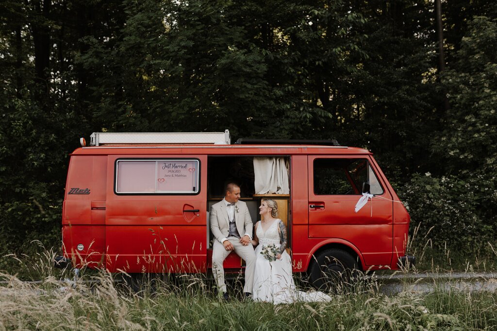 Ein Hochzeitspaar sitzt in einem alten Feuerwehr-Bulli und schaut sich verliebt
 an.