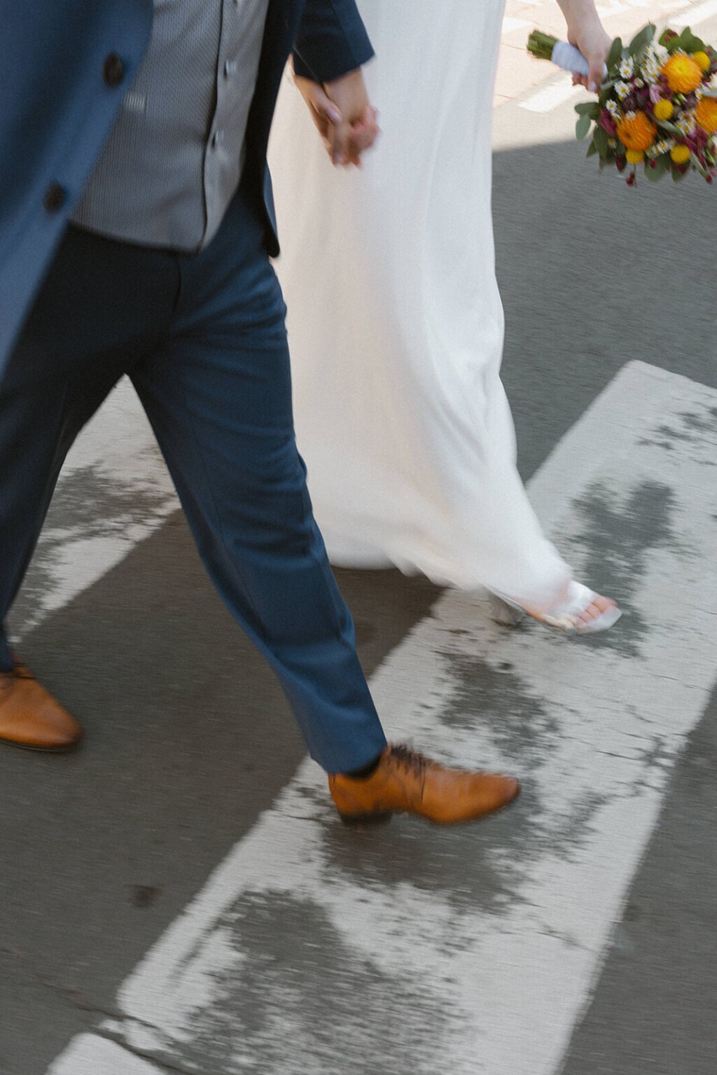 Ein Hochzeitspaar geht Händchen haltend über einen Zebrastreifen.