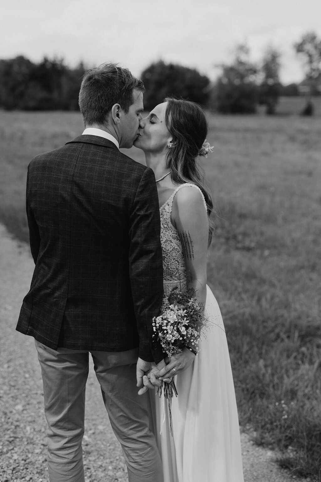 Ein Hochzeitspaar küsst sich auf einem Feldweg.