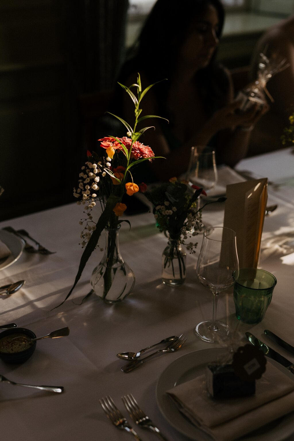 Mehrere Blumen in einer Vase auf einem feierlich gedeckten Hochzeitstisch. Die Abendsonne fällt von der Seite ein und trifft auf die Blumen.